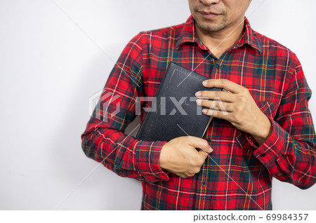 Believer man holding bible book on chest Believer man holding bible book on chest 69984357