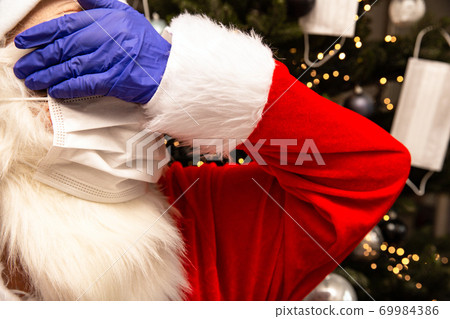 Santa Claus wearing a Face Mask and protective safety gloves for Covid-19, Santa standing by the Christmas tree unhappy about Coronavirus. Santa Claus wearing a Face Mask and protective safety gloves for Covid-19, Santa standing by the Christmas tree unhappy about Coronavirus. 69984386