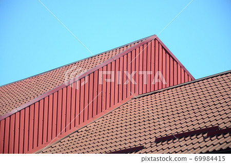 A fragment of a roof from a metal tile of dark red color. Quality Roofing A fragment of a roof from a metal tile of dark red color. Quality Roofing 69984415