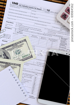 Composition of items lying on the 1040 tax form. Dollar bills, calculator, smartphone, paper clip and notepad. The time to pay taxes 69984562