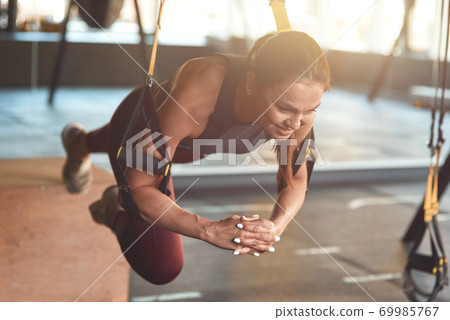 Working hard. Young athletic fitness woman in sportswear doing TRX workout at industrial gym, working out with fitness straps. Suspension training concept 69985767