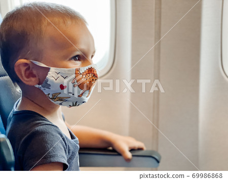 A small child on a seat on an airplane near the window in a protective mask.  Health and travel concept. 69986868