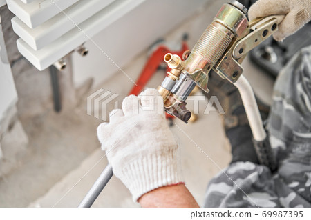 connection heating pipes to white Radiator in a new apartment under construction. Work As A Plumber, mounting water heating radiator on the white wall indoors connection heating pipes to white Radiator in a new apartment under construction. Work As A Plumber, mounting water heating radiator on the white wall indoors 69987395