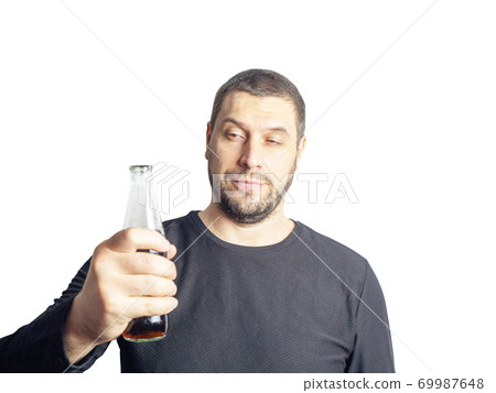 A dark-haired man with a beard in black clothes holds a bottle with a drink 69987648