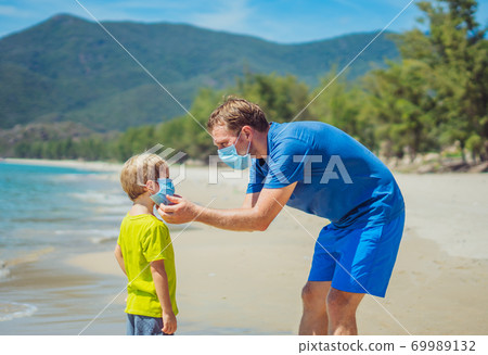 New normal reality era safety during COVID 19 Global pandemic. Father accompanies son putting on mask protect and prevent coronavirus even walking nature sand sea beach near forest park in sunny day New normal reality era safety during COVID 19 Global pandemic. Father accompanies son putting on mask protect and prevent coronavirus even walking nature sand sea beach near forest park in sunny day 69989132