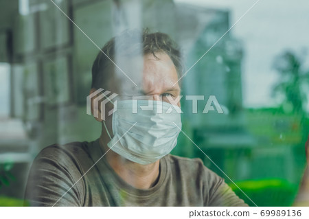Portrait Man wear white protective mask, looking outside through window, happy hope wink in smile eyes, recovery from the illness in home, self isolation due to global COVID 19 Coronavirus pandemic 69989136