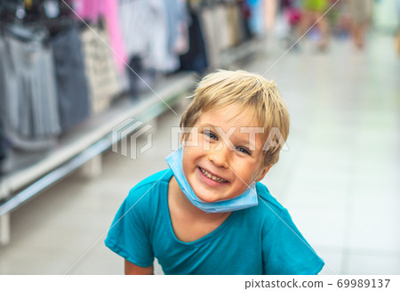 Close portrait cute smiling blue eyed freckled blond boy artistic facial expressions, gestures wearing sanitary face mask shopping supermarket. New normal safety health protection covid 19 quarantine Close portrait cute smiling blue eyed freckled blond boy artistic facial expressions, gestures wearing sanitary face mask shopping supermarket. New normal safety health protection covid 19 quarantine 69989137