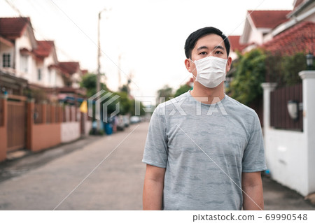 Young Asian man wearing a face protective mask in front of his house outdoors. Wearing a face mask before leaving home Young Asian man wearing a face protective mask in front of his house outdoors. Wearing a face mask before leaving home 69990548