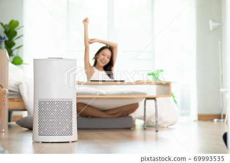 air purifier in living room for clean and fresh air with woman stretching hands and relax in background air purifier in living room for clean and fresh air with woman stretching hands and relax in background 69993535