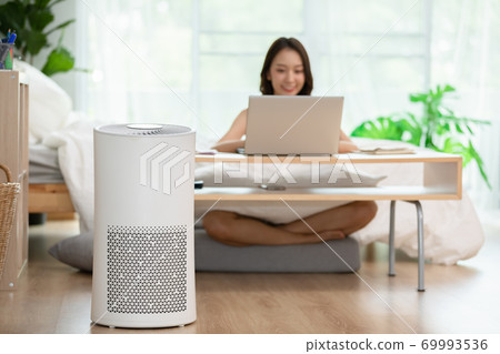 air purifier in living room for clean and fresh air with woman working with computer laptop and relax in background air purifier in living room for clean and fresh air with woman working with computer laptop and relax in background 69993536