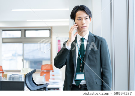 A young businessman standing with a smartphone in the office 69994187