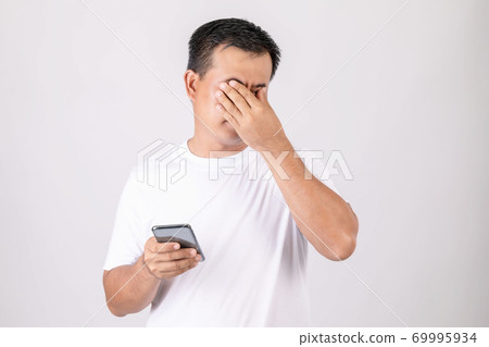 Eyestrain concept. Man touching his eyes because pain or hurt after using too much smartphone. Studio shot isolated on grey Eyestrain concept. Man touching his eyes because pain or hurt after using too much smartphone. Studio shot isolated on grey 69995934