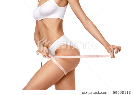 Slim tanned woman's body over gray background - waist measurement 69998118