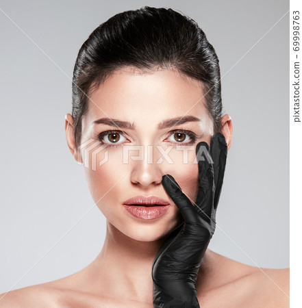 Woman is touching her face before plastic surgery. Adult girl checks a skin before botox injection. Beauty treatments. White woman in the black medical gloves. Face skin check before plastic surgery. 69998763