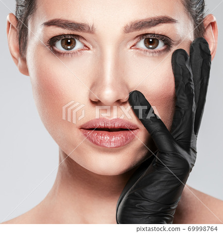 Woman is touching her face before plastic surgery. Adult girl checks a skin before botox injection. Beauty treatments. White woman in the black medical gloves. Face skin check before plastic surgery. Woman is touching her face before plastic surgery. Adult girl checks a skin before botox injection. Beauty treatments. White woman in the black medical gloves. Face skin check before plastic surgery. 69998764