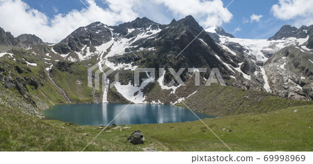 Panoramic view of turquoise blue mountain lake Grunausee in alpine landscape with green meadow and snow-capped mountain peaks. Tyrol, Stubai Alps, Austria, summer sunny day 69998969