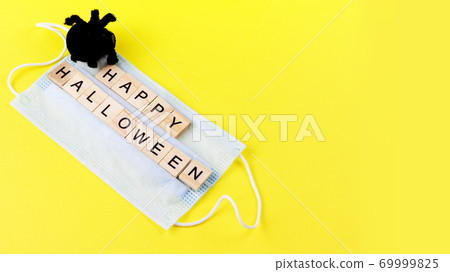 Black toy spider, medical mask and words Happy Halloween on yellow. Halloween background decor holiday concept Black toy spider, medical mask and words Happy Halloween on yellow. Halloween background decor holiday concept 69999825
