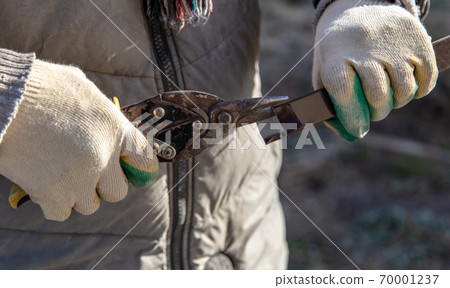 Worker cuts metal with scissors at a construction site Worker cuts metal with scissors at a construction site 70001237