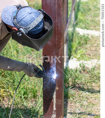 A worker welds metal for a fence. A worker welds metal for a fence. 70001583
