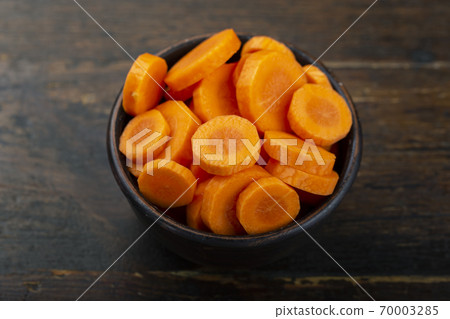 Sliced carrots in a bowl on a wooden background. Vegetable, ingredient and staple food. 70003285