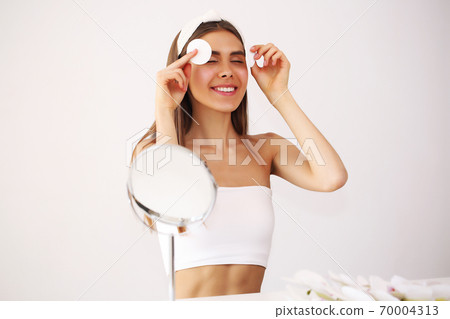 Young attractive woman standing in front of a mirror taking care of herself after a warm bath Young attractive woman standing in front of a mirror taking care of herself after a warm bath 70004313