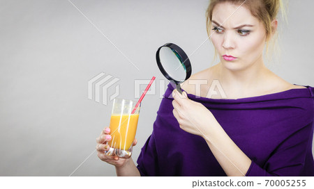 Woman holding magnifying glass investigating juice 70005255