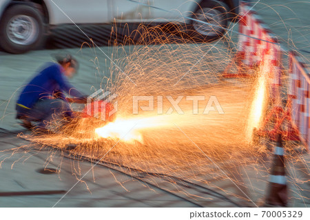 A man cuts steel with a red sparkle flying from cut metal material.  70005329