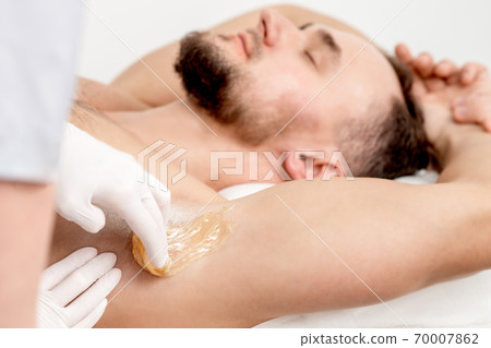 Cosmetologist applying wax paste on male armpit Cosmetologist applying wax paste on male armpit 70007862