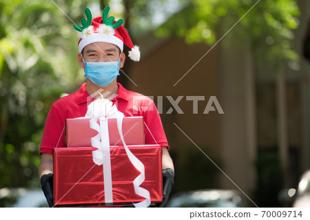 Asian delivery man wearing face mask and gloves and Christmas hat delivering present during COVID-19 Asian delivery man wearing face mask and gloves and Christmas hat delivering present during COVID-19 70009714