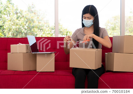 Happy young Asian entrepreneurs on a mask are packing boxes for delivering products to customers. Small business owner and success in online business concepts. Happy young Asian entrepreneurs on a mask are packing boxes for delivering products to customers. Small business owner and success in online business concepts. 70010184
