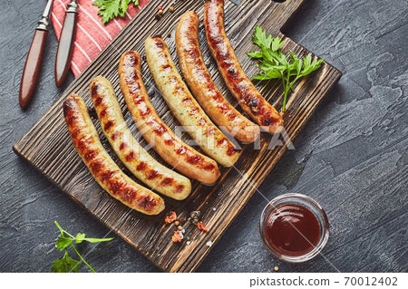 Tasty grilled pork sausages with spice and herbs on wooden cutting board in a close up view. Tasty grilled pork sausages with spice and herbs on wooden cutting board in a close up view. 70012402