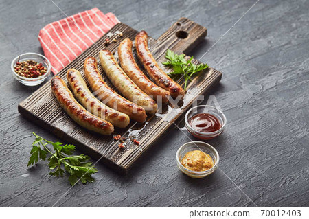 Tasty grilled pork sausages with spice and herbs on wooden cutting board in a close up view. Tasty grilled pork sausages with spice and herbs on wooden cutting board in a close up view. 70012403