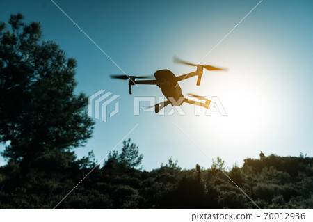 A silhouette of a Quadrocopter drone with the camera against the blue sky. A silhouette of a Quadrocopter drone with the camera against the blue sky. 70012936