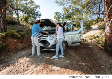 Man is looking to open car hood for troubleshoot car, next to him a worried woman. Transportation and vehicle concept. Man is looking to open car hood for troubleshoot car, next to him a worried woman. Transportation and vehicle concept. 70012937