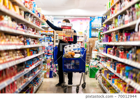 Full shopping cart, customer is stocking vital needs because of global chaos. Shopping with blur supermarket store products, interior background. Full shopping cart, customer is stocking vital needs because of global chaos. Shopping with blur supermarket store products, interior background. 70012944