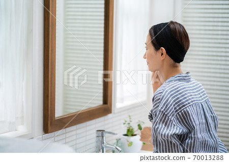 洗她的面孔的一名中年婦女在洗手間。 70013288