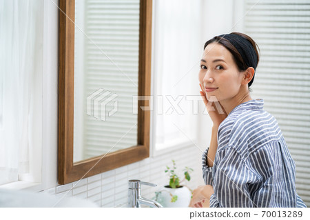 洗她的面孔的一名中年婦女在洗手間。 洗她的面孔的一名中年婦女在洗手間。 70013289