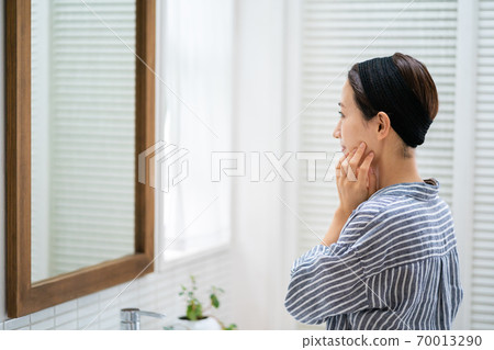 洗她的面孔的一名中年婦女在洗手間。 洗她的面孔的一名中年婦女在洗手間。 70013290