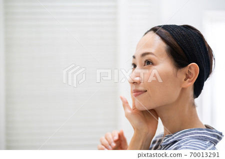 洗她的面孔的一名中年婦女在洗手間。 洗她的面孔的一名中年婦女在洗手間。 70013291