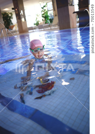 little girl in a pool cap and blue swimsuit learns to swim in the pool little girl in a pool cap and blue swimsuit learns to swim in the pool 70013549