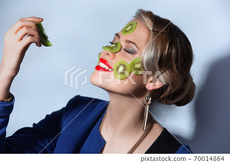 Fashion photo of woman posing with slices of kiwi on her face Fashion photo of woman posing with slices of kiwi on her face 70014864