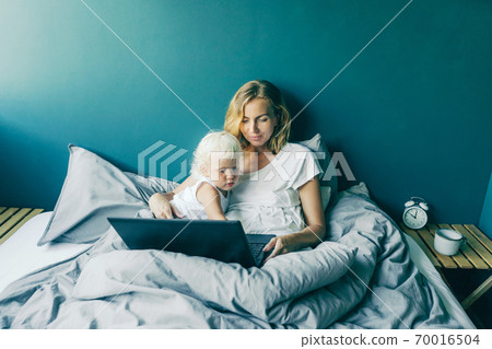 In the morning in bed, mom and daughter look at the laptop screen. 70016504