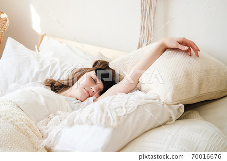 Young beautiful girl lying in comfortable bed wearing sleep mask in the morning at cozy room. Concept of rest at home, sleep, insomnia, self-isolation, stay home during quarantine, pandemic. Young beautiful girl lying in comfortable bed wearing sleep mask in the morning at cozy room. Concept of rest at home, sleep, insomnia, self-isolation, stay home during quarantine, pandemic. 70016676