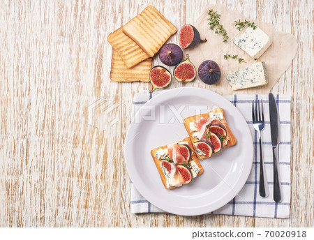 Open sandwich with blue cheese, prosciutto and fresh figs on a white ceramic plate, top view. 70020918