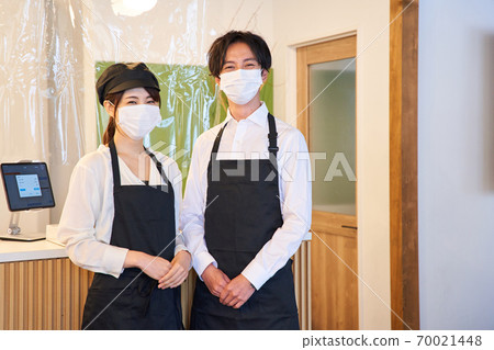 A clerk standing in front of a cash register in a cafe with a vinyl partition 70021448
