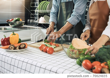 Two young asian couples are helping each other and enjoying cooking in the kitchen. Two young asian couples are helping each other and enjoying cooking in the kitchen. 70024835