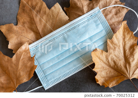 Covid-19 protective mask on dry autumn leaves background 70025312