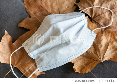 Covid-19 protective mask on dry autumn leaves background 70025313