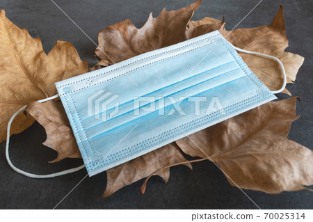 Covid-19 protective mask on dry autumn leaves background 70025314