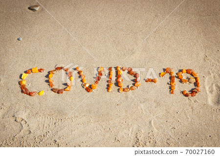 Inscription Covid-19 made of amber stones on sand at beach. Safe holidays 70027160